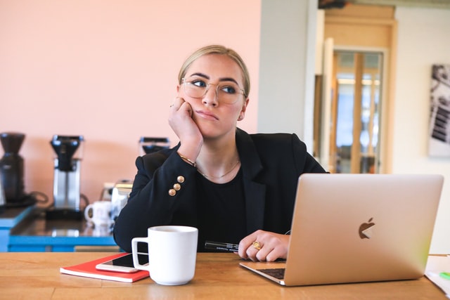 Blonde woman sitting at a desk with a coffee mug and a laptop in front of her researching the biggest challenges for real estate agents in NYC