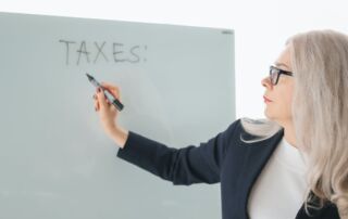 A woman is writing “taxes” on a whiteboard as one of the hurdles in NYC real estate